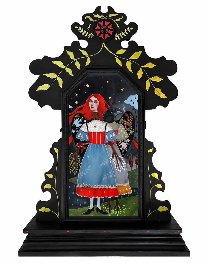 Folk-inspired artwork by Aunia Kahn with a red-haired woman and a raven-like figure within an ornate, dark wooden frame.