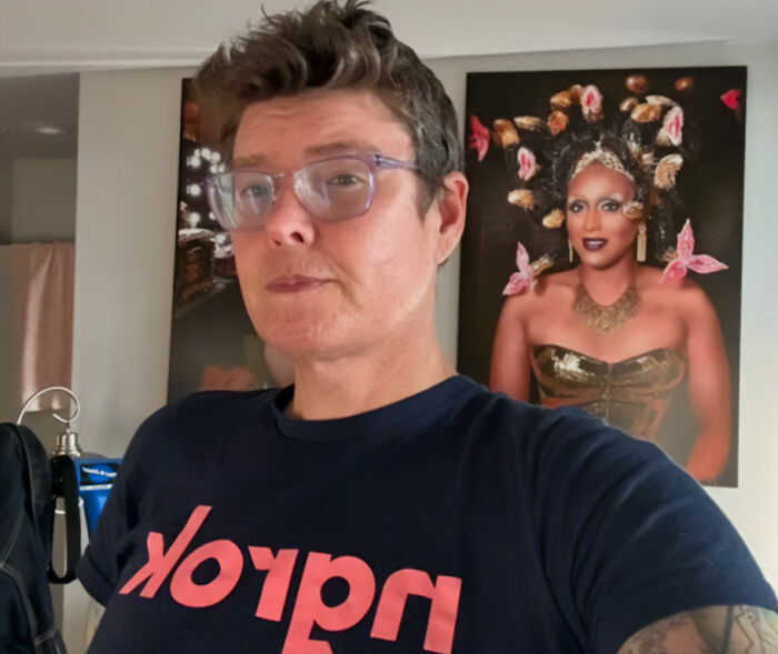 A Trans American recounts horrors after fleeing US for European asylum center, standing indoors with drag queen art. A Trans American recounts horrors after fleeing US for European asylum center, standing indoors with drag queen art.