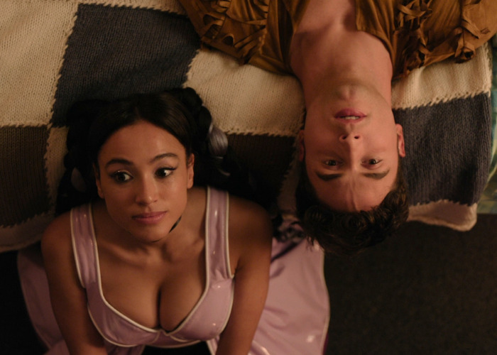 A Gen Z couple, one woman with dark hair and a man, lying on a patterned blanket, looking up.