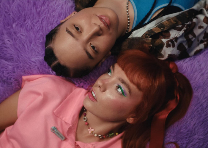 Two Gen Z individuals, one with braids and the other with red hair, lying on a purple fuzzy surface.