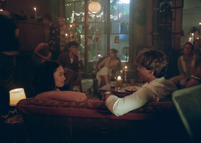 A group of Gen Z people gathered in a dimly lit room, with two individuals conversing on a couch.