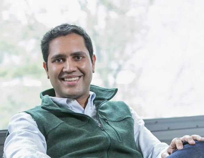 CEO who went viral for firing 900 employees via Zoom smiles, wearing a green vest.