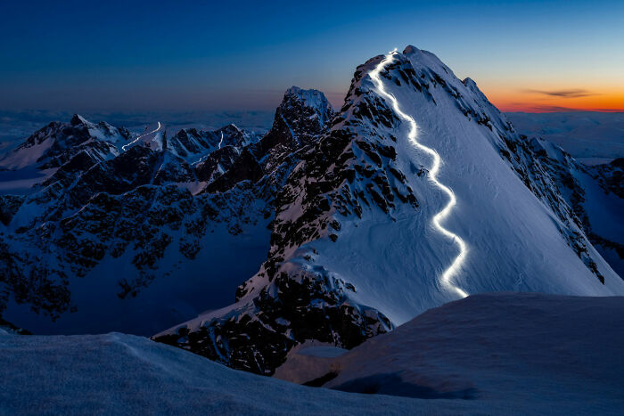 A dramatic snowy mountain peak with a glowing light trail ascending, a stunning image from the Nature Photography Festival.