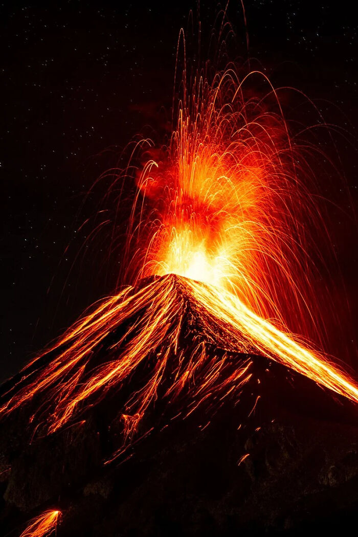 A volcano erupts with fiery lava streams against a dark sky, a powerful moment among winning images of the world.