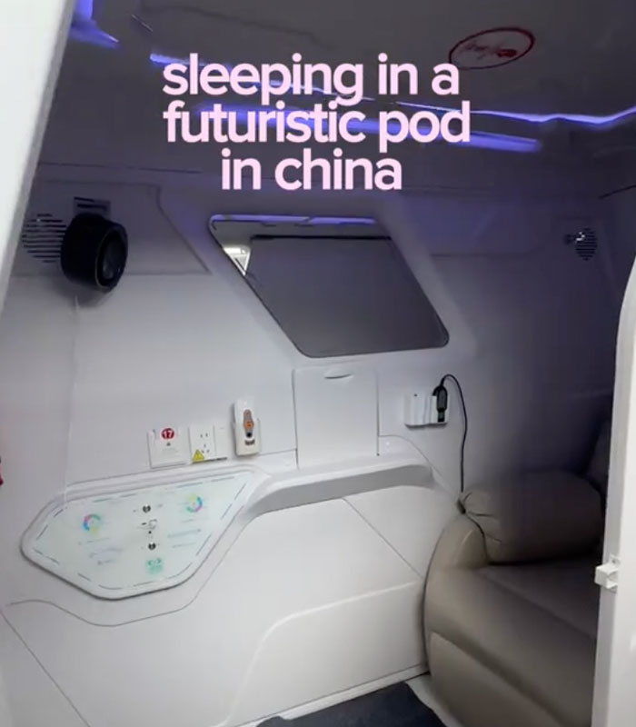 Interior of a futuristic sleeping pod in a Chinese airport, showing a bed, small desk, and charging outlets. Interior of a futuristic sleeping pod in a Chinese airport, showing a bed, small desk, and charging outlets.
