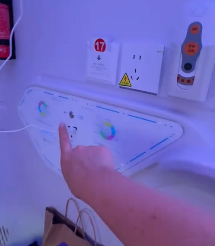 A hand adjusting controls inside a futuristic sleeping pod in a Chinese airport, next to power outlets. A hand adjusting controls inside a futuristic sleeping pod in a Chinese airport, next to power outlets.