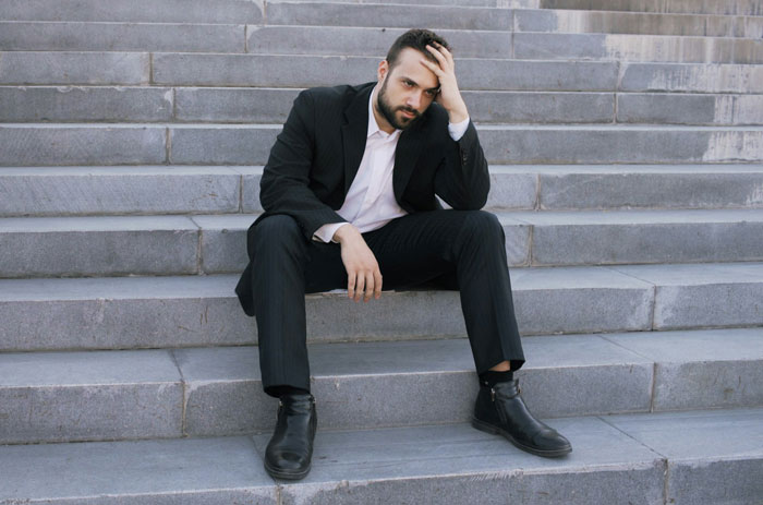 A man in a suit looks distraught while sitting on steps, representing a husband discovering his wife cheats. A man in a suit looks distraught while sitting on steps, representing a husband discovering his wife cheats.