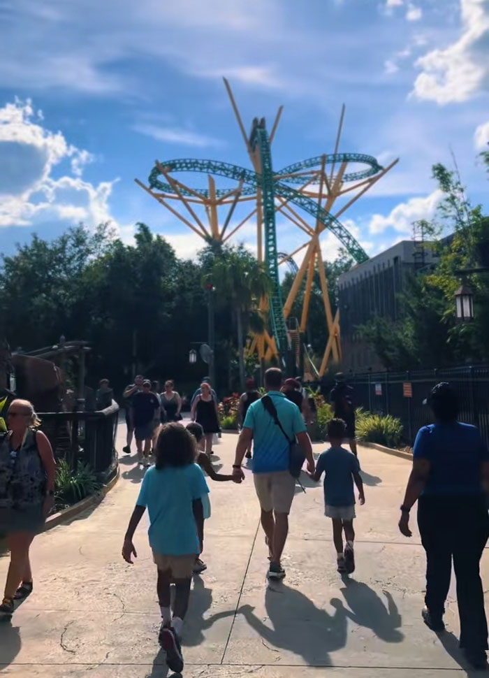 Family and kids walking through a theme park, enjoying their mornings with a roller coaster in the background. Family and kids walking through a theme park, enjoying their mornings with a roller coaster in the background.