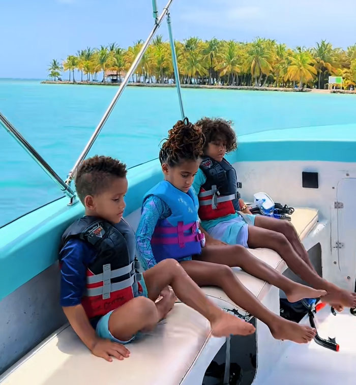 Three kids wearing life vests on a boat, enjoying their mornings on the water with palm trees in the background. Three kids wearing life vests on a boat, enjoying their mornings on the water with palm trees in the background.