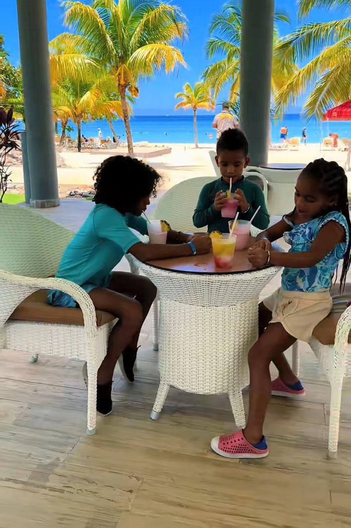Three kids enjoying drinks at a table by the beach, spending mornings reading and exercising. Three kids enjoying drinks at a table by the beach, spending mornings reading and exercising.
