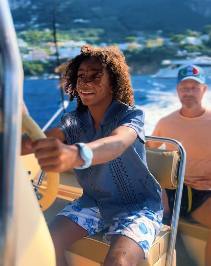 A child steering a boat with an adult in the background, representing kids spending mornings reading and exercising and then enjoying activities. A child steering a boat with an adult in the background, representing kids spending mornings reading and exercising and then enjoying activities.