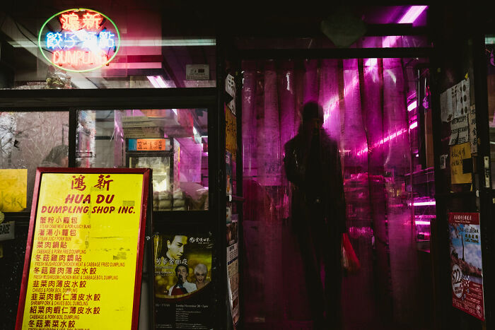 Vivid street photography capture of a person walking through a bright pink doorway with neon signs nearby.