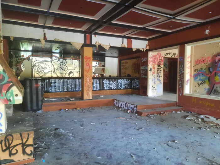 An abandoned, graffiti-covered room with a bar and debris on the floor, ideal for urban exploration with location.