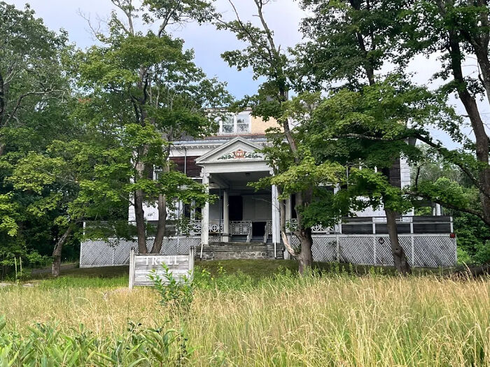 An old, white house with green trees around it, a captivating sight for urban exploration with location.