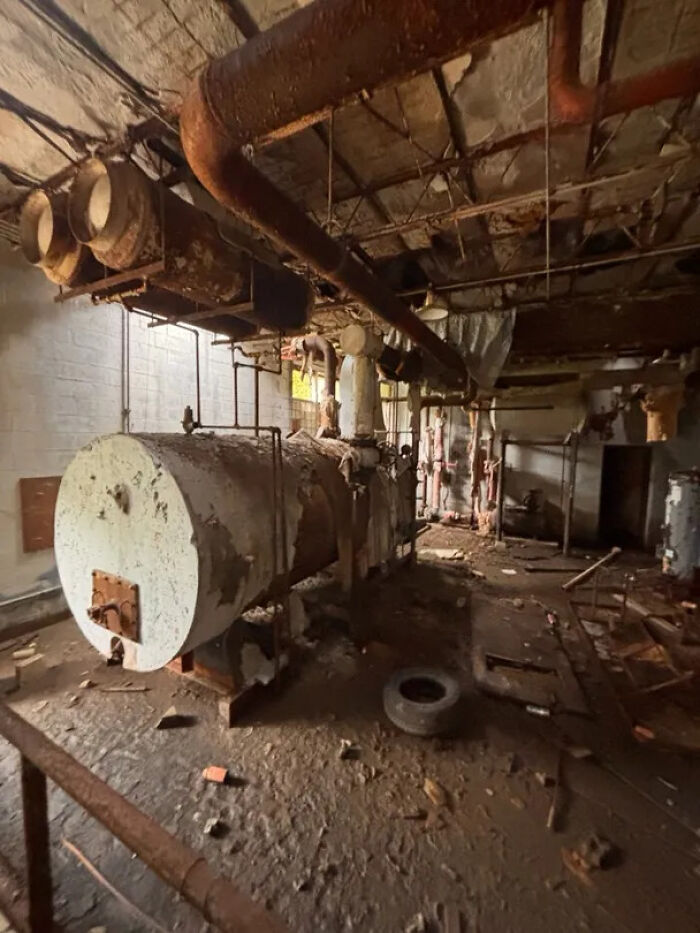 Urban exploration of a dilapidated factory interior with large rusty pipes and industrial equipment.
