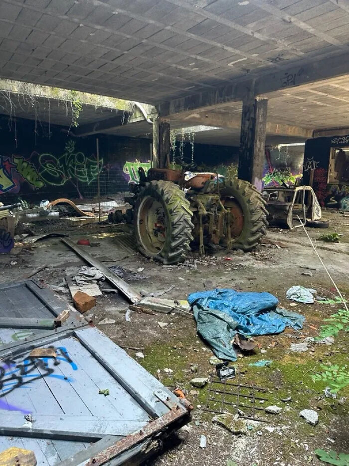 An abandoned and rusty tractor covered in graffiti and debris inside a derelict building, a classic urban exploration scene.