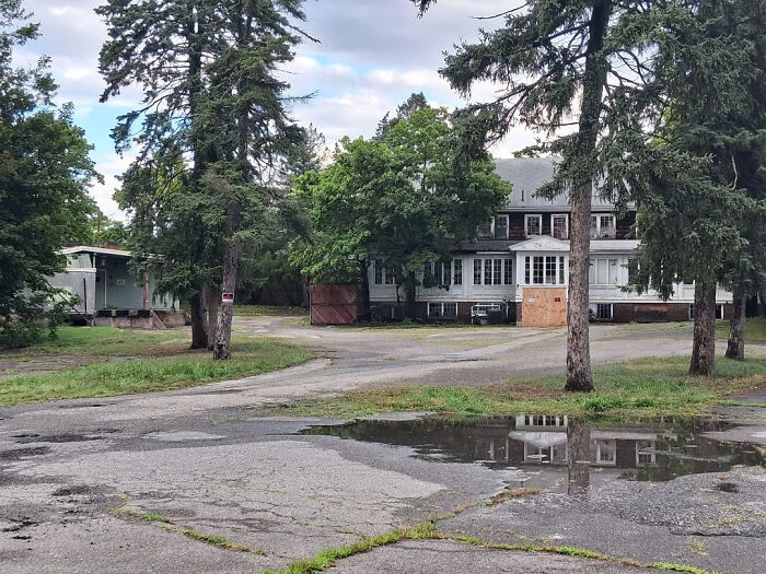 Urban exploration of an abandoned house with a circular driveway and puddles, surrounded by trees.