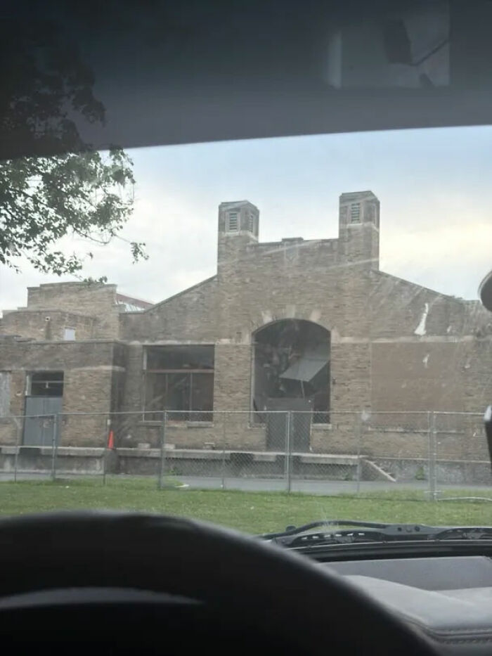A brick building with boarded-up windows and an arched entrance, seen through a car windshield, for urban exploration with location.