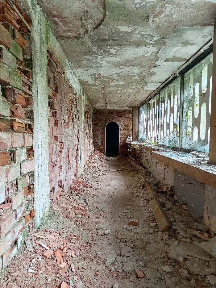 A dark, crumbling hallway with exposed brick walls, a collapsed ceiling, and debris on the floor, perfect for urban exploration.