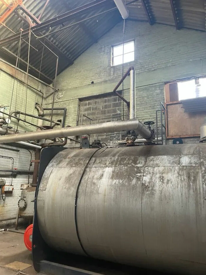 An abandoned industrial boiler room with large metal tanks and pipes, showing decay, ideal for urban exploration.