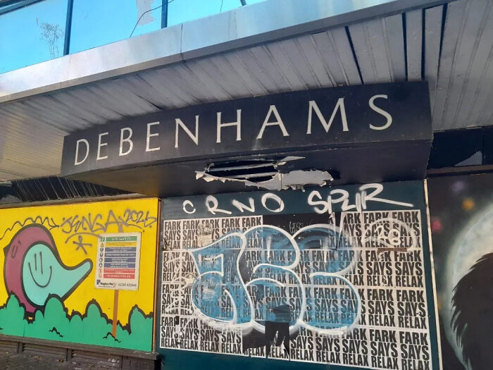 Urban exploration of an abandoned Debenhams sign with graffiti and posters, part of a closed store.