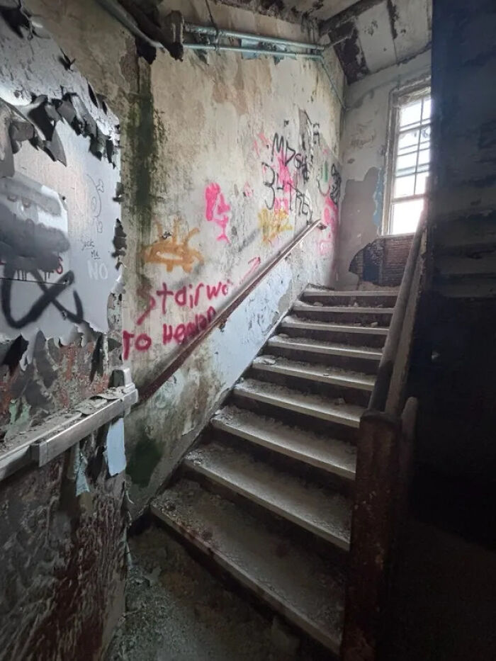 Urban exploration of a dilapidated staircase with peeling paint and graffiti in an abandoned building.