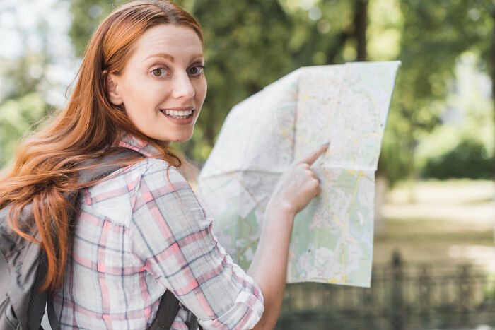A young European woman holding a map and smiling, ready to answer absurd American questions about travel.