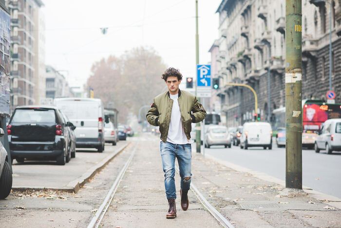 A young European man walks confidently on tram tracks in a city, embodying European style often subject to absurd American questions.