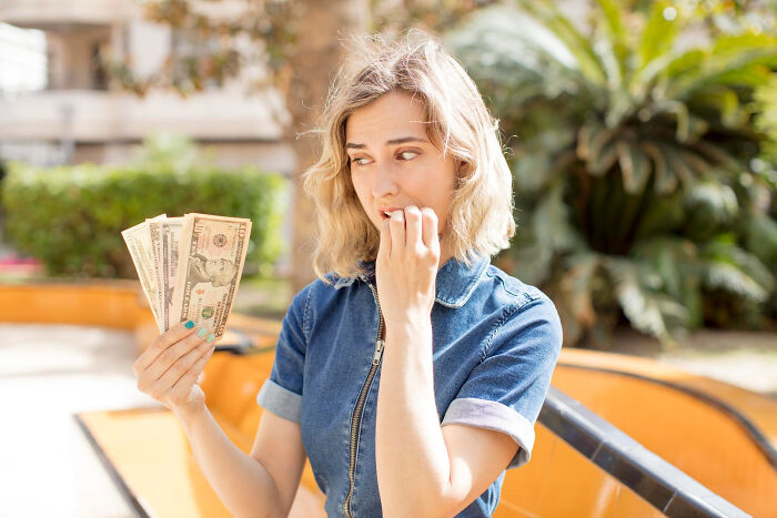 Concerned woman holding American dollar bills, illustrating financial anxieties related to absurd American questions.