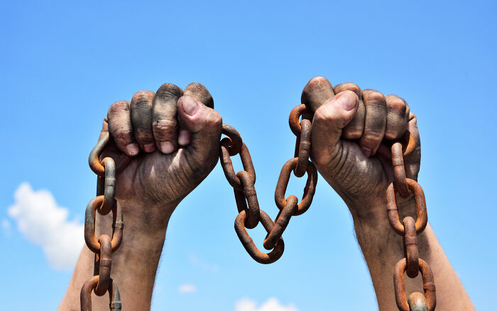 Two dirty hands breaking a rusty chain against a blue sky, symbolizing freedom from absurd questions.