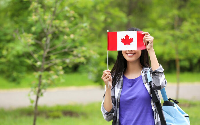 A young woman holding a Canadian flag over her face, representing absurd American questions to Europeans.