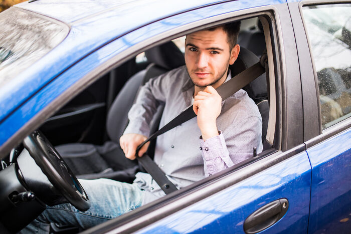 A man in a blue car buckling his seatbelt, representing American driving habits.