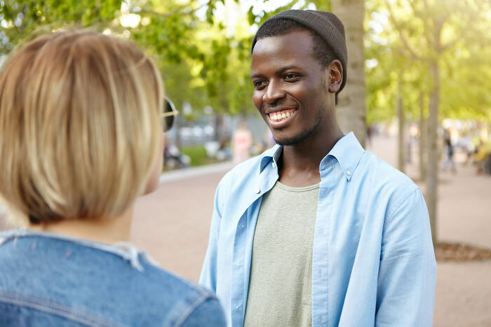 A smiling American man talking to a European woman in a park, discussing absurd questions.