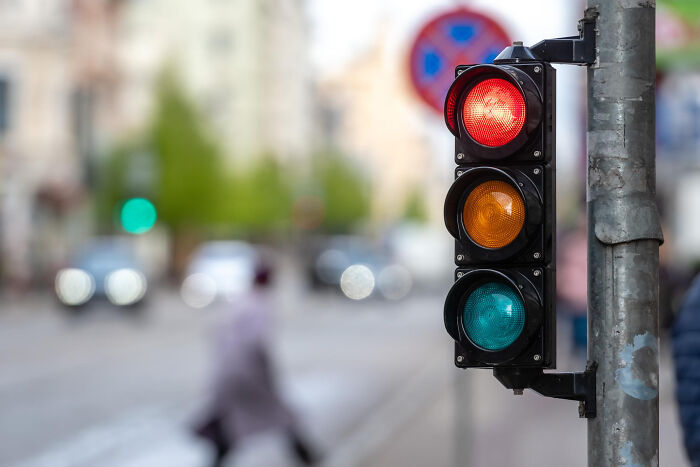 A red traffic light with a blurred street background, symbolizing American transportation questions.