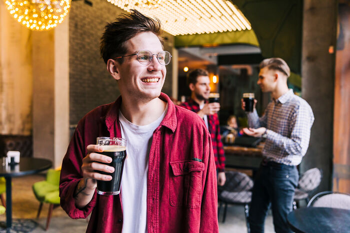 A smiling American man holding a beer, possibly discussing absurd questions asked to Europeans.