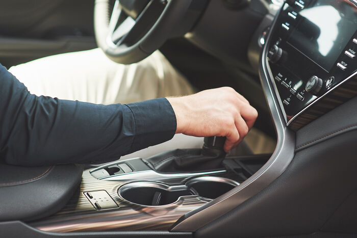 A hand shifting gears in a car, representing different driving habits that lead to absurd American questions.