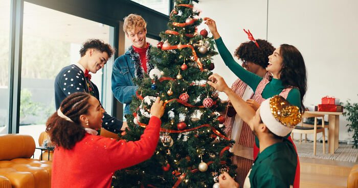 A diverse group of friends decorating a Christmas tree, highlighting a European holiday tradition that might invite absurd American questions.