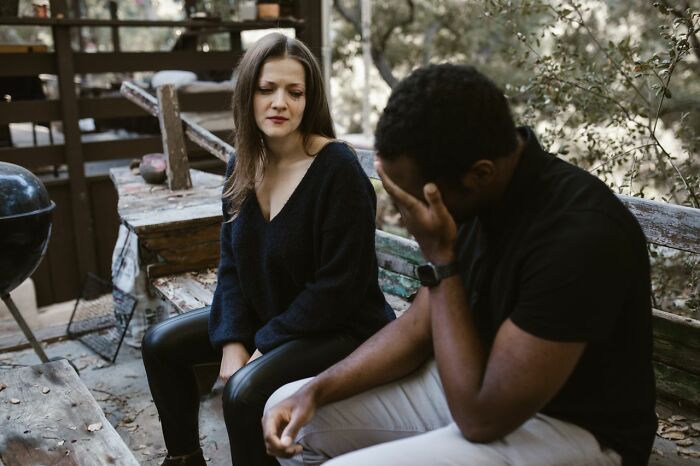 A sad woman looks away from a man covering his face with his hands. This image depicts ridiculous reasons people stop speaking to each other.