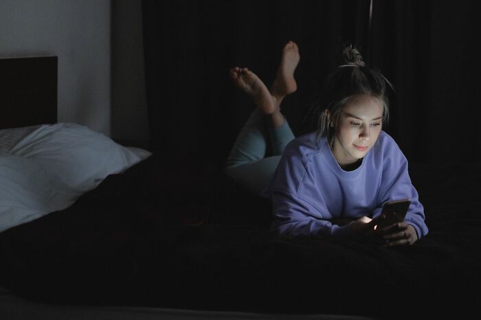 A young woman in a dark room looks at her phone, reflecting a glow on her face. This image illustrates ridiculous reasons people stop speaking to each other.