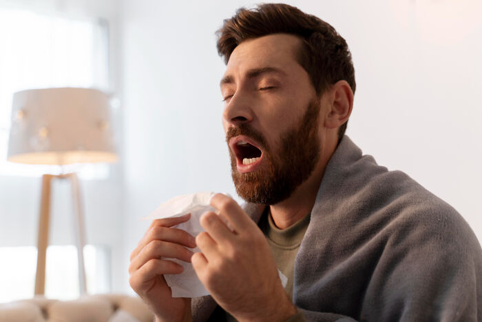 A man with a beard sneezing into a tissue, representing how ridiculous reasons can leave others seeing red.