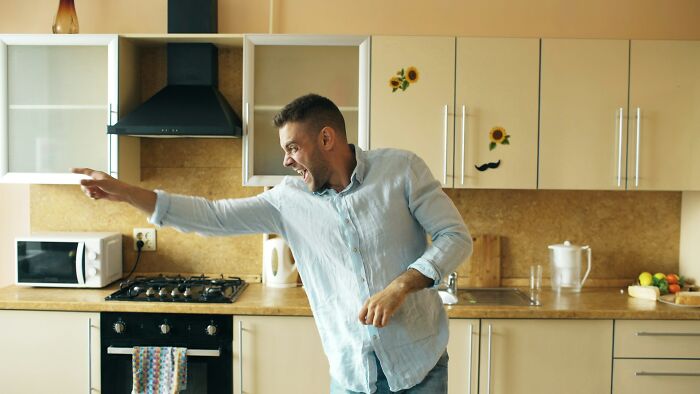 A man in a light blue shirt dancing in a kitchen, expressing ridiculous reasons for someone seeing red.
