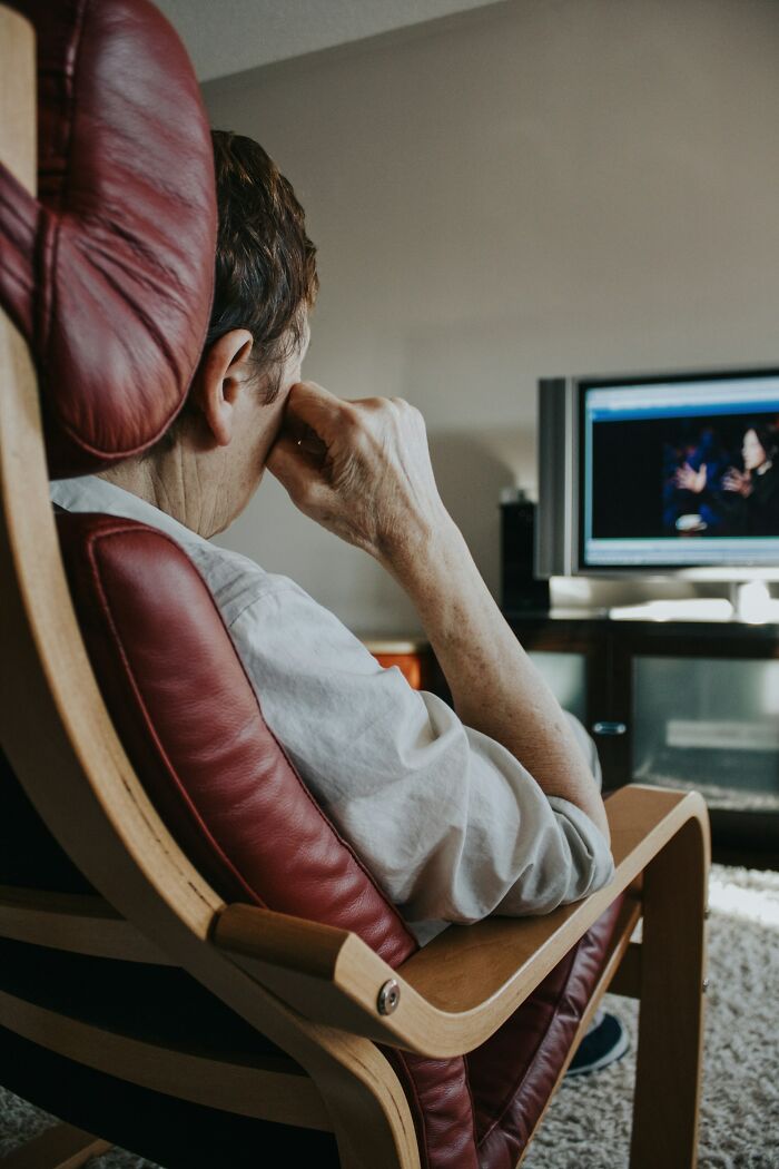 An older person sitting in a red armchair, watching TV, illustrating a person seeing red over reasons.