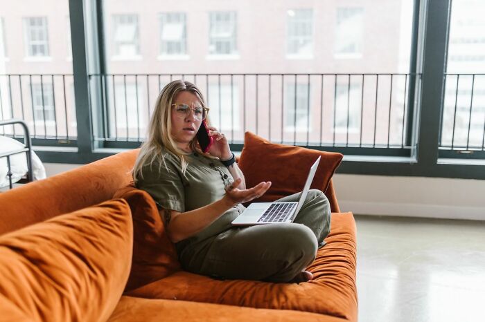 A woman on a sofa, on the phone and laptop, expresses frustration, showcasing ridiculous reasons for conflict.
