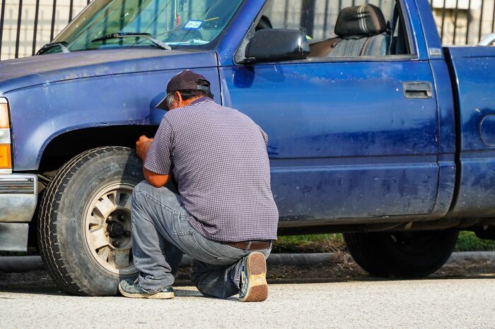A man kneels by a blue truck, working on a tire, depicting ridiculous reasons people get upset.