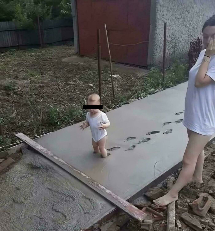 A baby standing in freshly poured wet cement, leaving footprints, a classic challenging moment for parents.