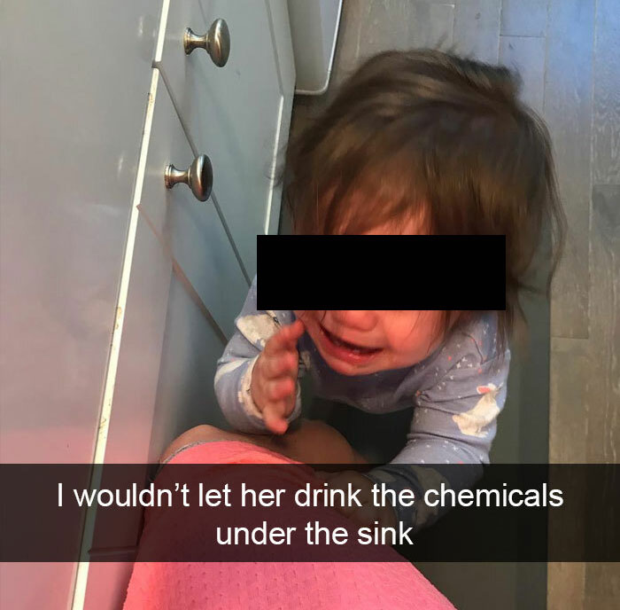 A crying toddler reaching under a sink, a relatable parenting scenario of preventing children from danger.