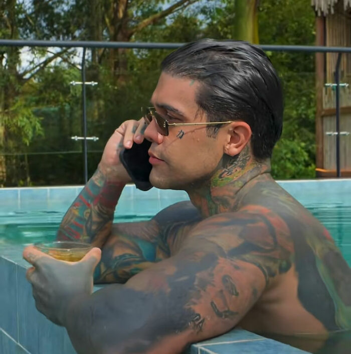 Tattooed influencer in a pool, talking on the phone and holding a drink, enjoying sweet karma.