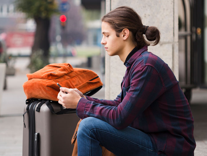 A young man looking at his phone, next to his luggage. He refuses to give inheritance to his sister adopted by stepmom. A young man looking at his phone, next to his luggage. He refuses to give inheritance to his sister adopted by stepmom.