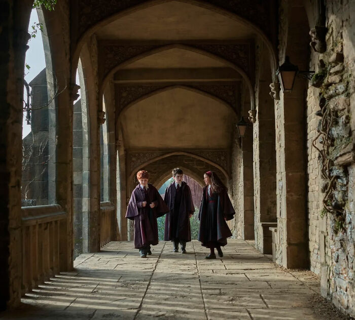 Three young individuals in cloaks walking through an archway, representing the Harry Potter series.