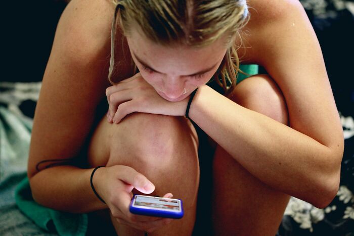 A young woman with wet hair, in a crouched position, intently looks at her phone, depicting questionable Instacart shopper incidents.